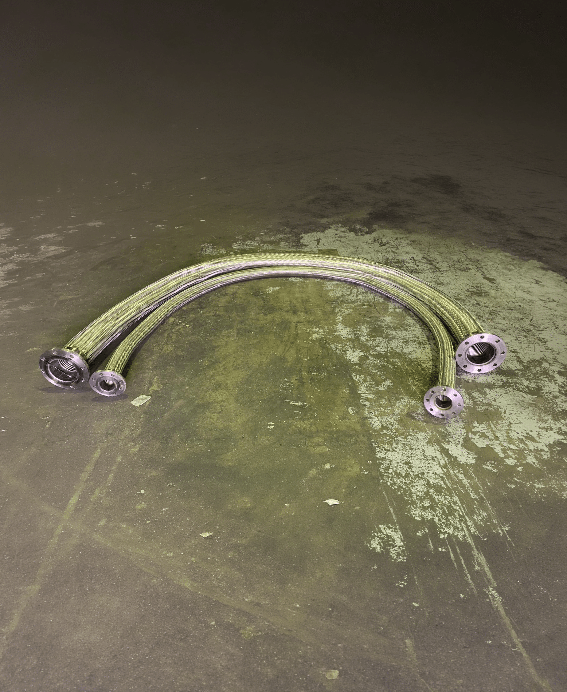 metalic hose asse-Edit Four metallic braided hoses with flanged ends placed on a textured concrete floor.