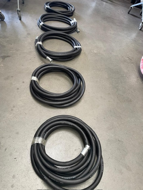 Five coiled black hoses are laid out in a row on a smooth concrete floor.